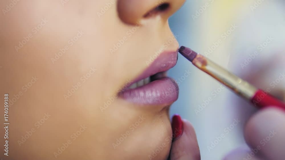 Closeup view of a professional makeup artist applying lipstick on model's lips working in beauty fashion industry. Closeup view of an artist's hand using special brush. Slowmotion Closeup view of a professional makeup artist applying lipstick on model's lips working in beauty fashion industry. Closeup view of an artist's hand using special brush. Slowmotion