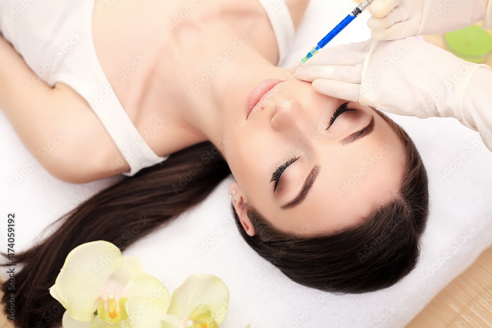 Hands of cosmetologist making injection in face, lips. Young woman gets beauty facial injections in salon. Face aging, rejuvenation and hydration procedures. Aesthetic cosmetology. Close up. Hands of cosmetologist making injection in face, lips. Young woman gets beauty facial injections in salon. Face aging, rejuvenation and hydration procedures. Aesthetic cosmetology. Close up.