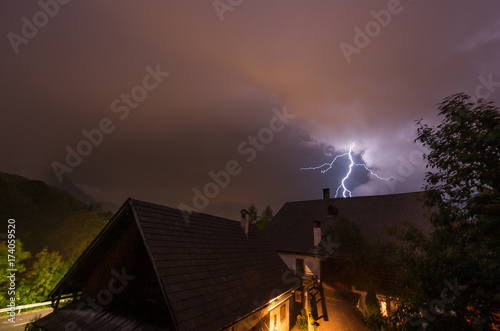 Flash during a thunderstorm at night behind a farming house