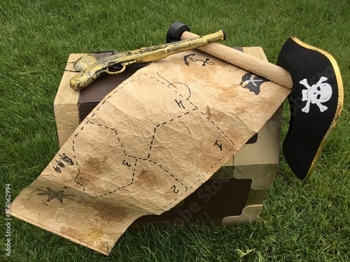 An old treasure map, a pirate hat, a gun and a treasure chest on the lawn photo