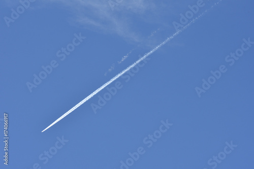 A jet plane flying overhead diagonally with condensation trail.