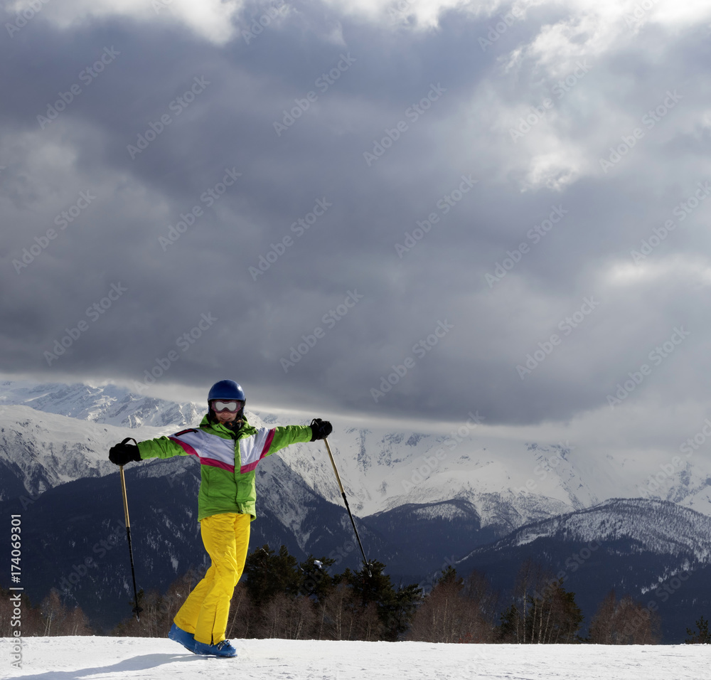 Happy young skier with ski poles in sun mountains and cloudy gray sky before storm Happy young skier with ski poles in sun mountains and cloudy gray sky before storm