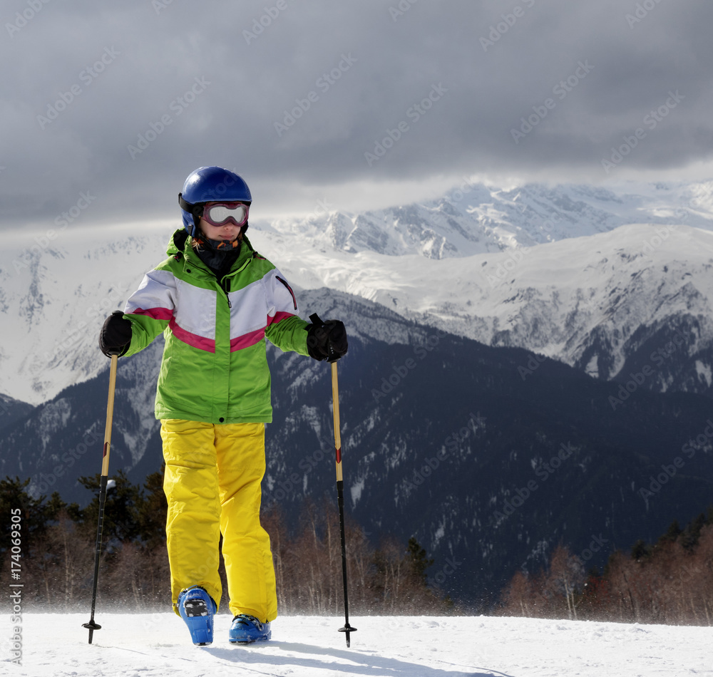 Young skier with ski poles in sun mountains and gray sky before storm