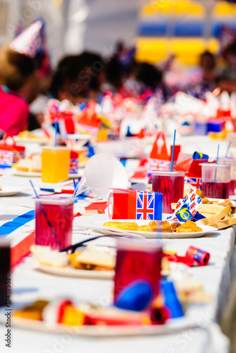 Children sit at long tables with red, white and blue party accessories at a Royal event street party