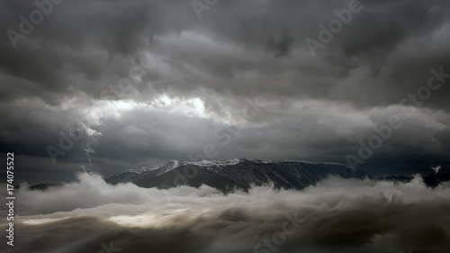 The top of the mountain between two levels of clouds during a storm.