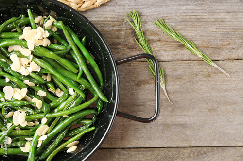 Frying pan with delicious green beans and almond on wooden background