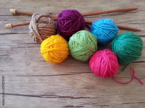 Multicolored yarn balls and wooden needles for knitting on wood background 