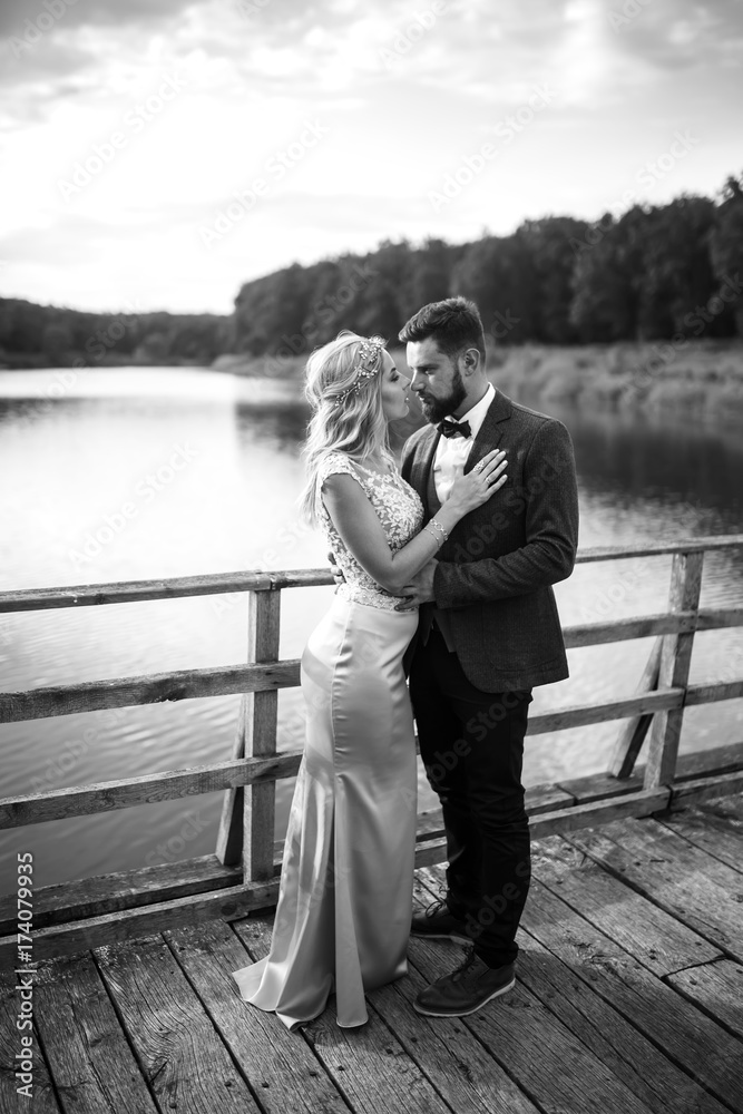 Stylish couple of happy newlyweds posing in the park on their wedding day. Perfect couple bride, groom posing and kissing.black and white.

