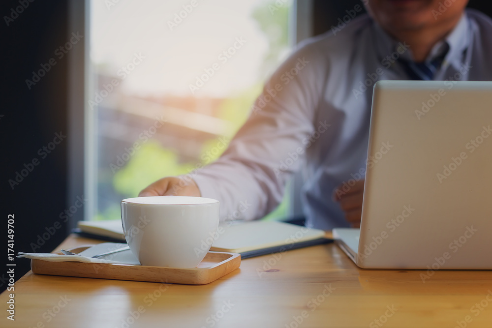 The photo closs up the hands of a businessman who is sitting with his laptop and sipping his coffee happily in his office. The photo closs up the hands of a businessman who is sitting with his laptop and sipping his coffee happily in his office.