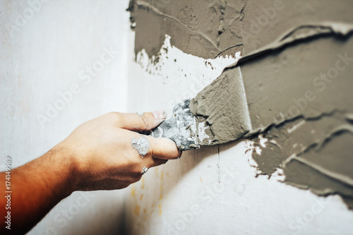 Painting worker puttied wall using a paint spatula hand closeup.