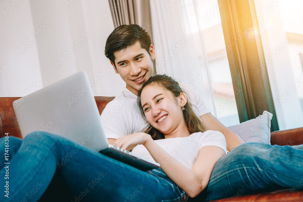 Teen Asian couple looking at laptop computer use on leather sofas in their beautiful home. Teen Asian couple looking at laptop computer use on leather sofas in their beautiful home.