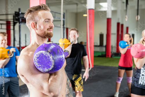 Male Instructor Lifting Kettlebell With Clients In Gym