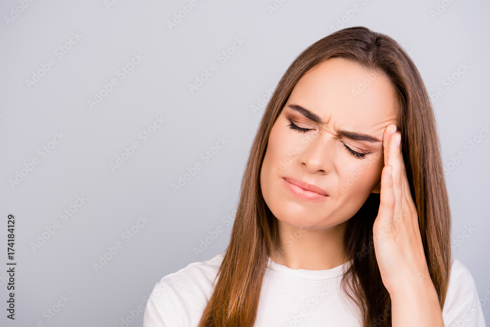 Strong migraine. Struggling beautiful young lady with strong pain grimace. She is wearing casual white outfit, standing on pure background, massaging her temples, worried Strong migraine. Struggling beautiful young lady with strong pain grimace. She is wearing casual white outfit, standing on pure background, massaging her temples, worried
