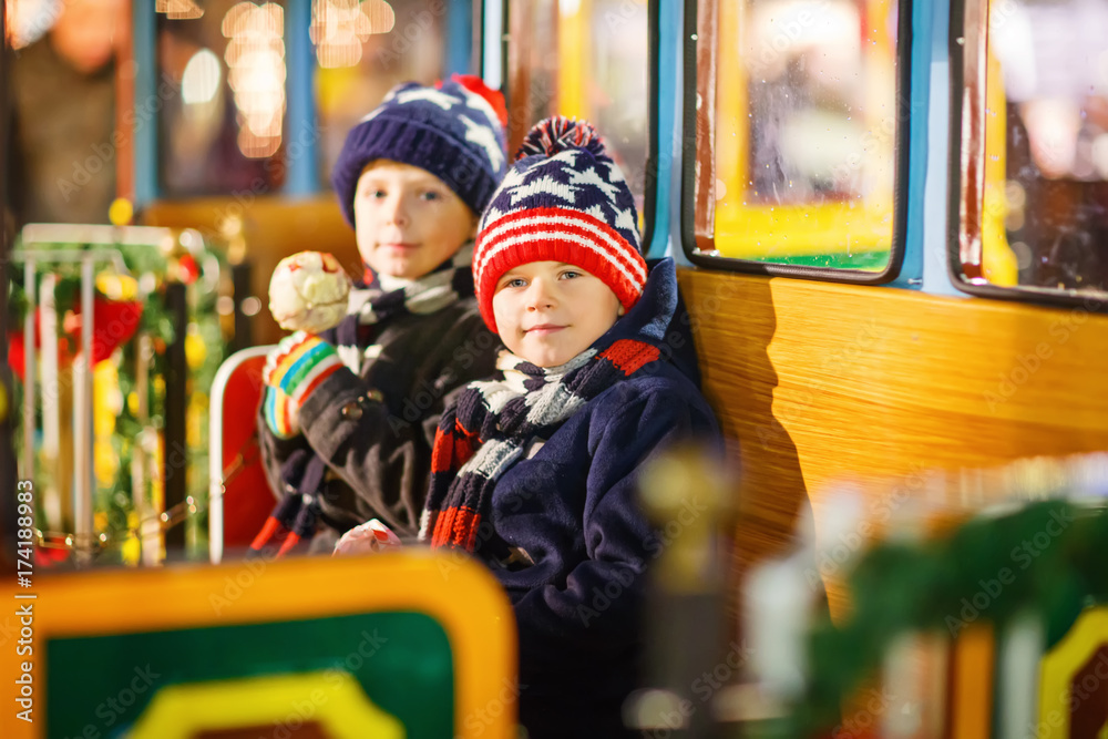 Obraz premium Two little kids boys on carousel at Christmas market