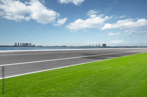 empty asphalt road and meadow with cityspace in blue sky