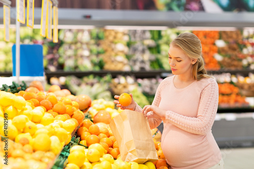 pregnant woman with bag buying oranges at grocery