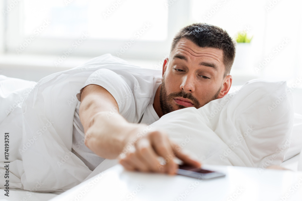 young man reaching for smartphone in bed young man reaching for smartphone in bed
