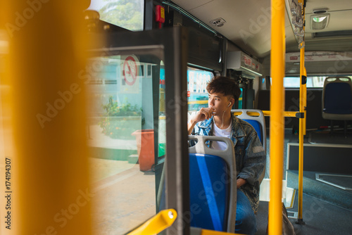 Asian man sitting in city bus, listening to music and looking through window.