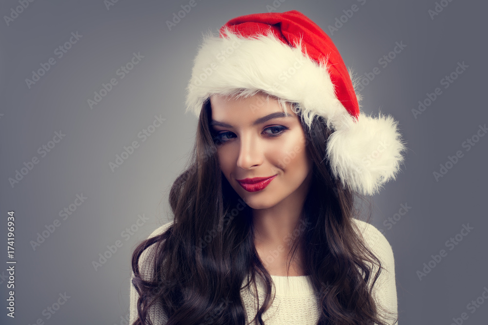 Christmas Portrait of Beautiful Smiling Woman in Red Santa Hat. New year Fashion Model Brunette with Makeup and Healthy Wavy Hair Christmas Portrait of Beautiful Smiling Woman in Red Santa Hat. New year Fashion Model Brunette with Makeup and Healthy Wavy Hair