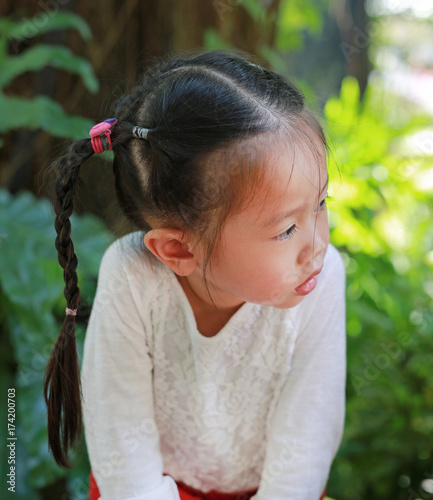 Adorable little asian girl looking out and sitting in the garden with background of tropical trees in the park.