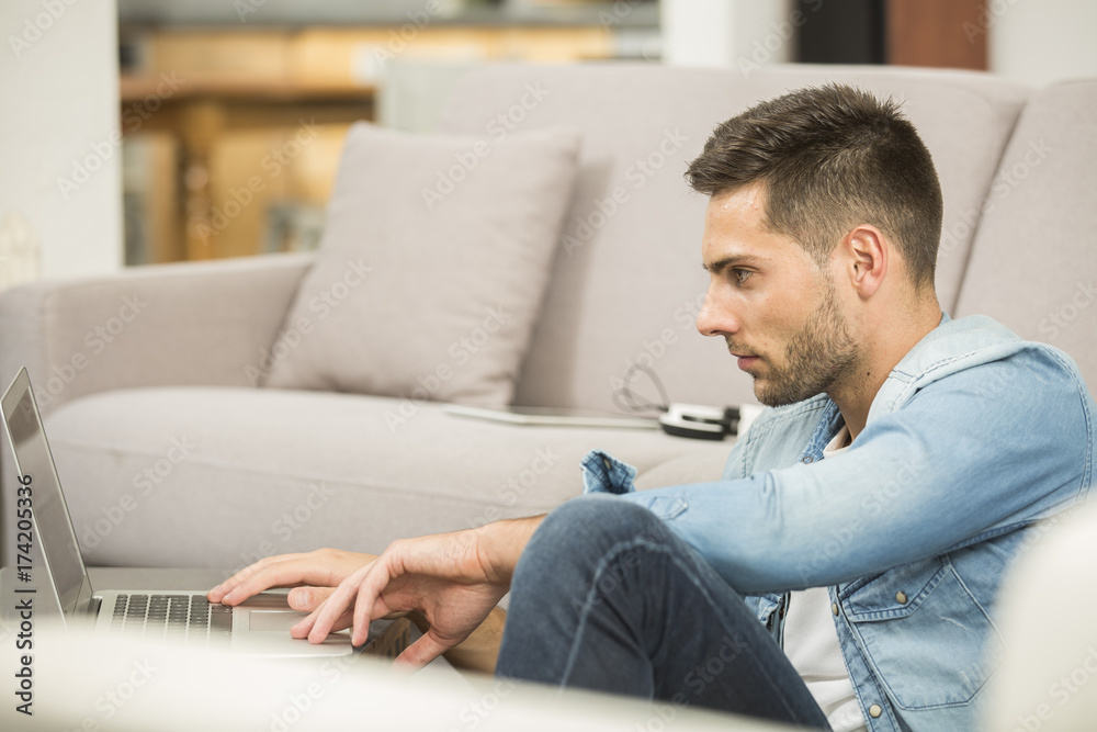 Fototapeta premium Young man in living-room using laptop computer