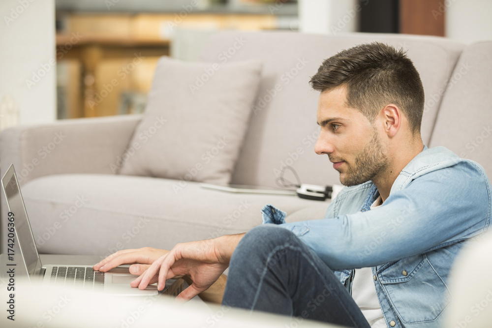 Young man in living-room using laptop computer Young man in living-room using laptop computer