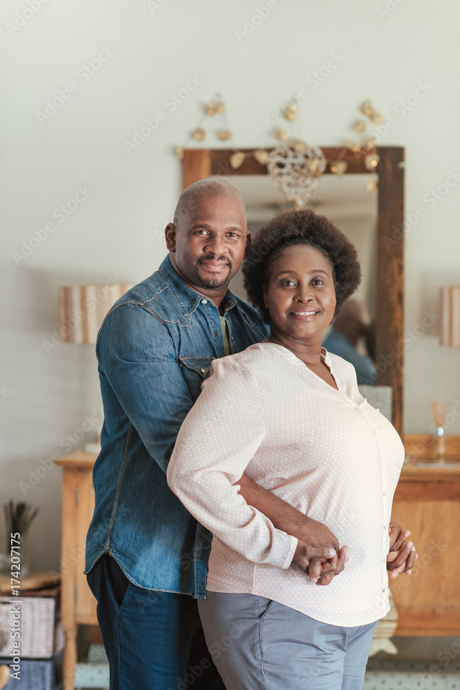 Smiling African couple standing lovingly together in their living room Smiling African couple standing lovingly together in their living room