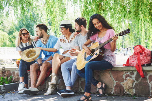 Group of happy friends with guitar. While one of them is playing guitar and others are giving him a round of applause photo