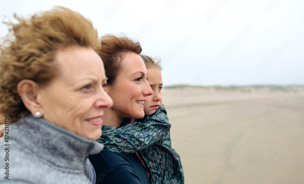 Closeup of three generations female looking at sea on the beach in autumn. Background focus on young woman and child Closeup of three generations female looking at sea on the beach in autumn. Background focus on young woman and child
