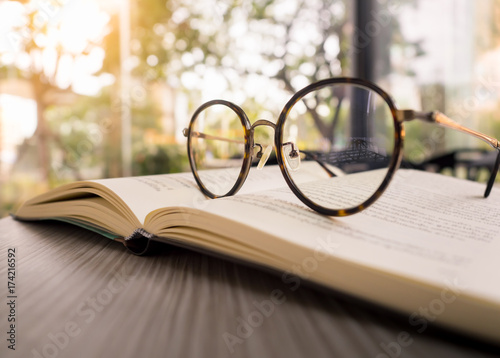 Fotografie Reading books concept, a glasses on old book on wooden desk in the morning with