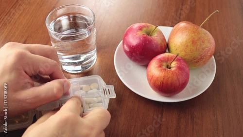 Human hand taking medicines, vitamins or supplements from the plastic box on wooden table photo