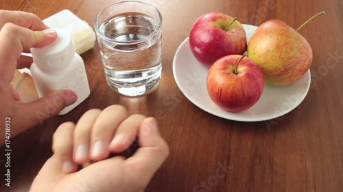 Human hand taking medicines, vitamins or supplements from the plastic box on wooden table photo