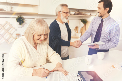 Cheerful aged woman signing papers
