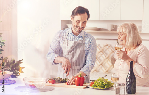 Cheerful adult man cooking with his aged mother