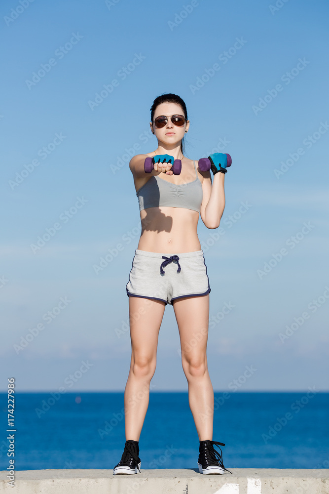 Girl with dumbbells exercising on embankment Girl with dumbbells exercising on embankment