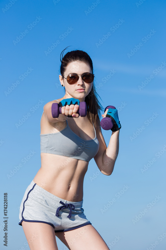 Girl with dumbbells exercising against sky Girl with dumbbells exercising against sky