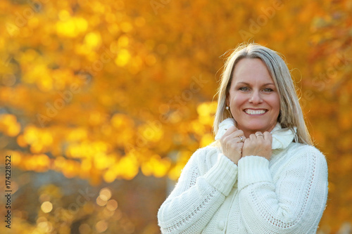 Happy mature woman in front of golden autumn leaves