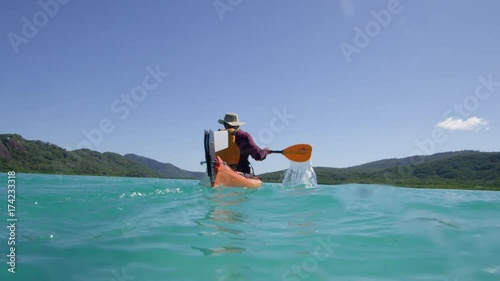 A slow motion wide shot of a man kayaking that already crossed the camera shot under a sunny day.