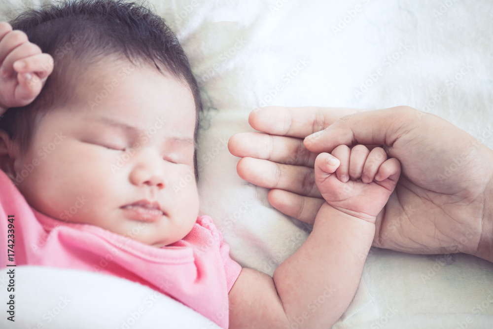Mother hand holding asian newborn baby girl hand while she sleeping with love Mother hand holding asian newborn baby girl hand while she sleeping with love