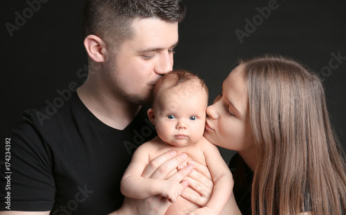 Happy young family holding newborn on black background