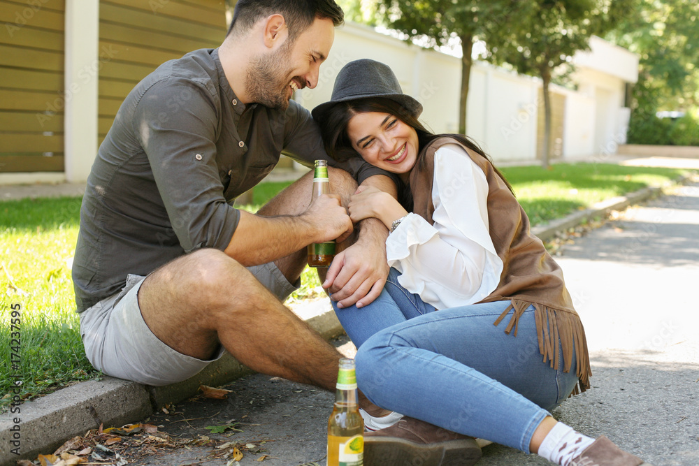 Young couple sitting in park and holding bottle of drink.