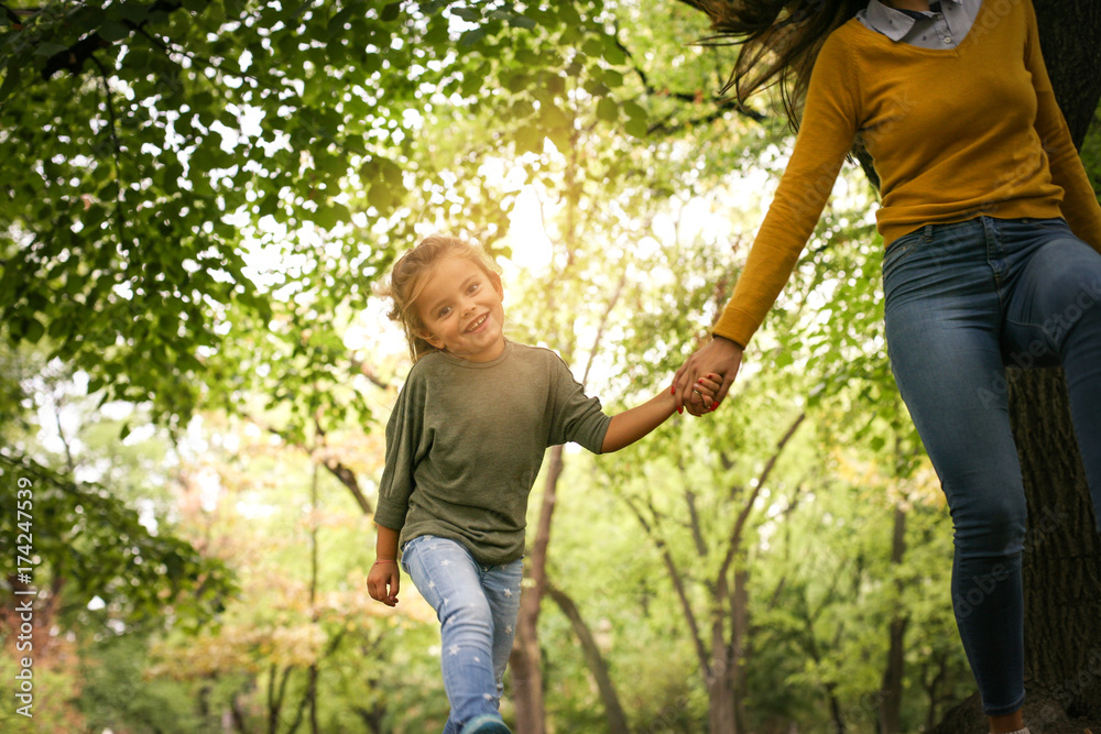 Fototapeta premium Mother an daughter in meadow. Mother and daughter holding hands and running together trough park.