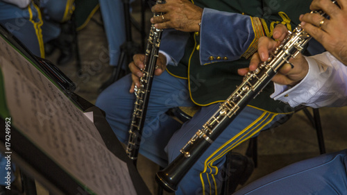 Dettaglio di suonatori di tromba durante un  esibizione ad un concerto di musica classica. Sono tutti vestiti con giacca e pantaloni blu mentre gli strumenti sono dorati. Sul leggio sta lo spartito.