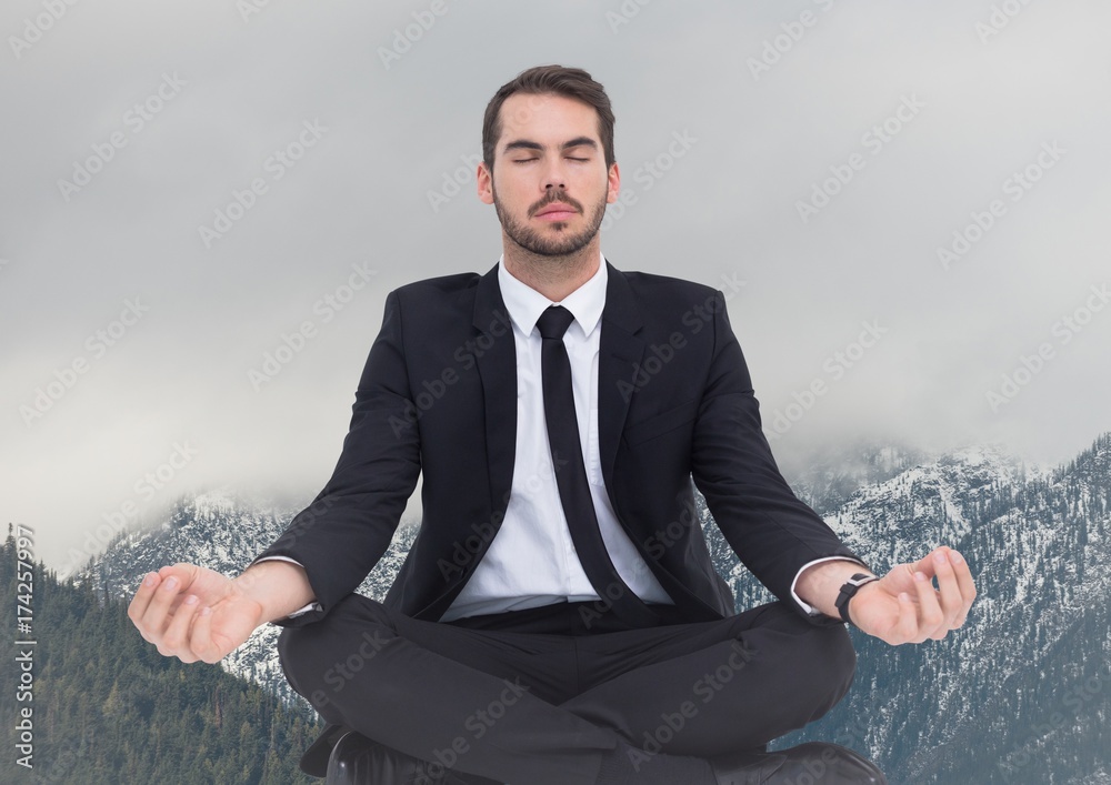 Business man meditating against snowy mountains Business man meditating against snowy mountains