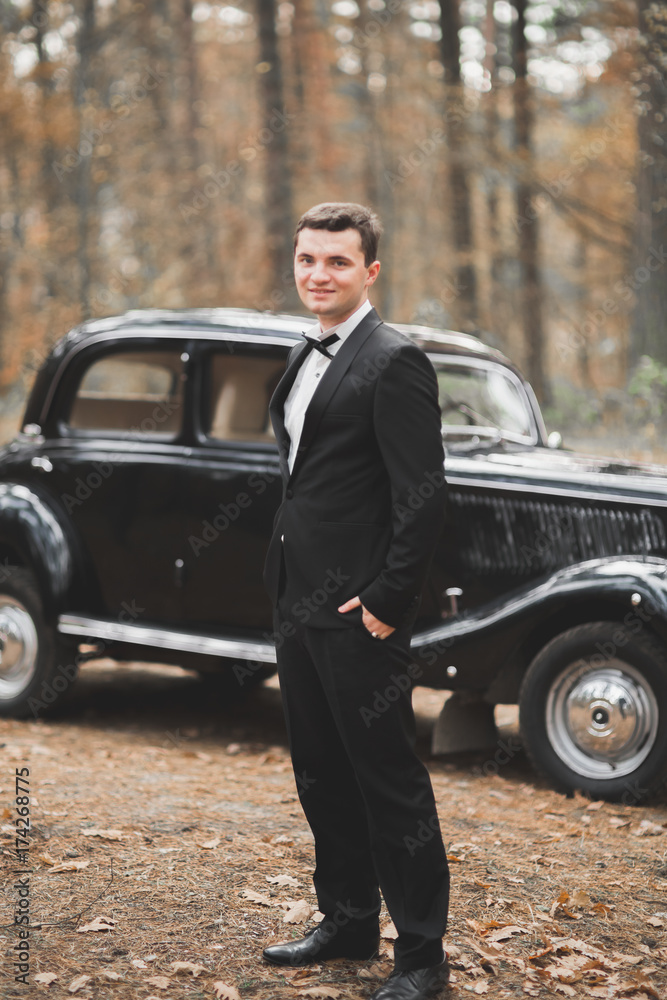 Handsome groom at wedding smiling and waiting for bride near retro car