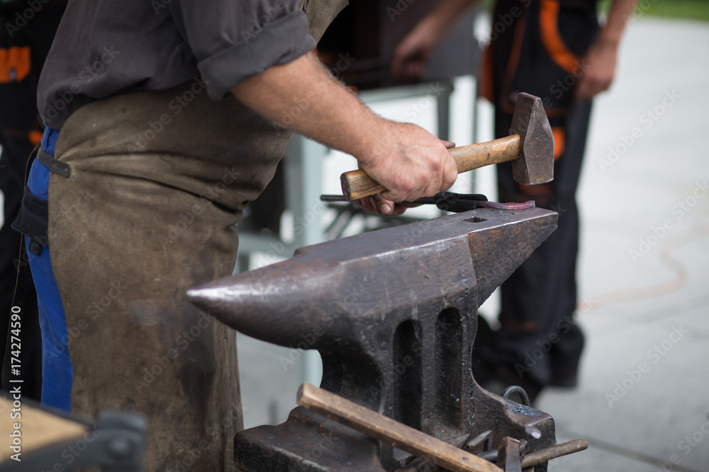 The blacksmith manually forging the molten metal on the anvil in smithy with spark fireworks The blacksmith manually forging the molten metal on the anvil in smithy with spark fireworks
