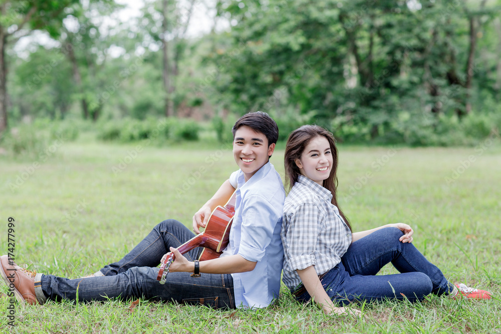 Young man playing guitar and sitting on the grass with his girlfriend Young man playing guitar and sitting on the grass with his girlfriend