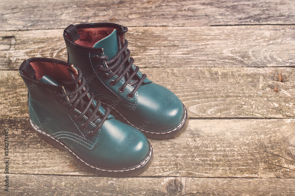 Boy's leather modern boots on dark wooden background.