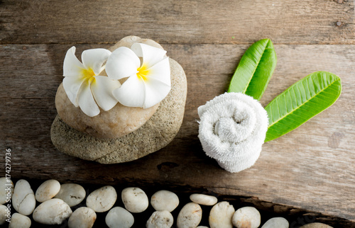 Fototapeta Naklejka Na Ścianę i Meble -  White flower and leafs with big and tiny stone and towel on wood table for health spa advertisement and presentation