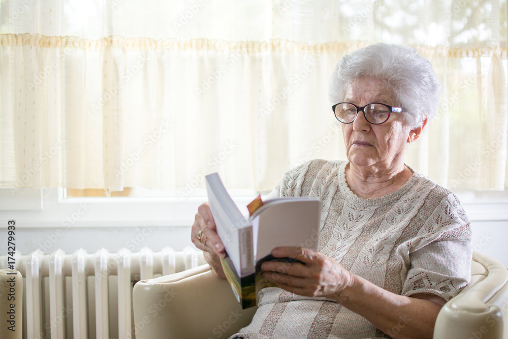 Senior woman reading book while relaxing on armchair at home. Senior woman reading book while relaxing on armchair at home.
